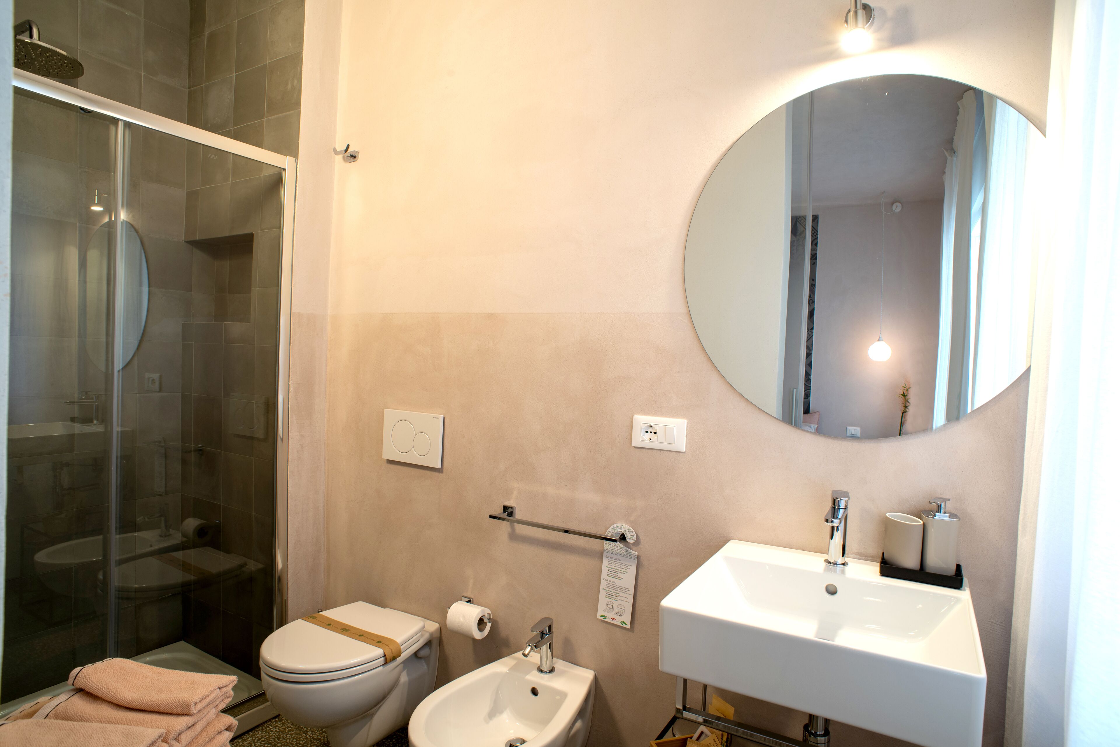 Un baño moderno con ducha de vidrio, inodoro, bidé, lavamanos y un espejo grande.