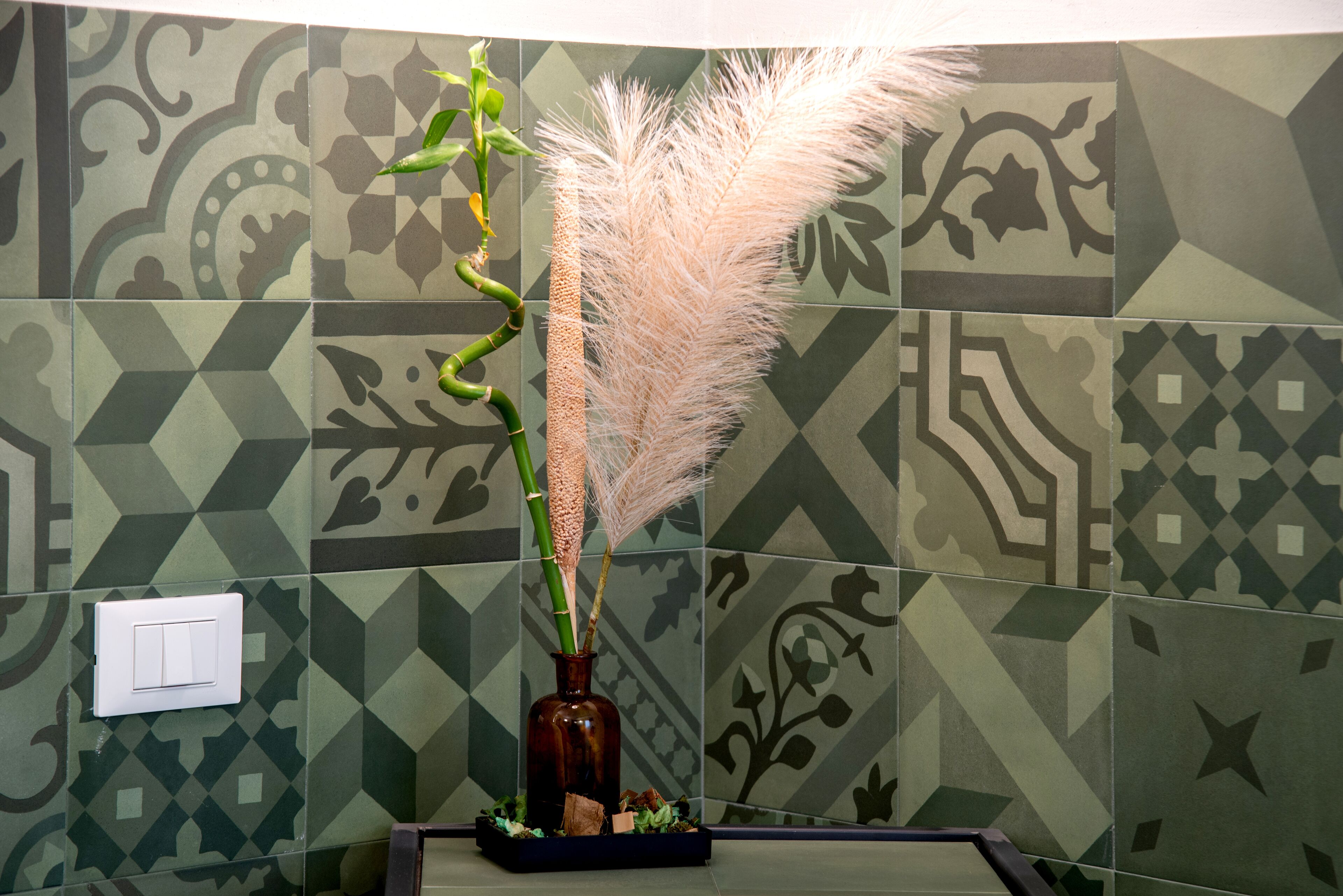 A bathroom with patterned tiles and a vase with pampas grass.