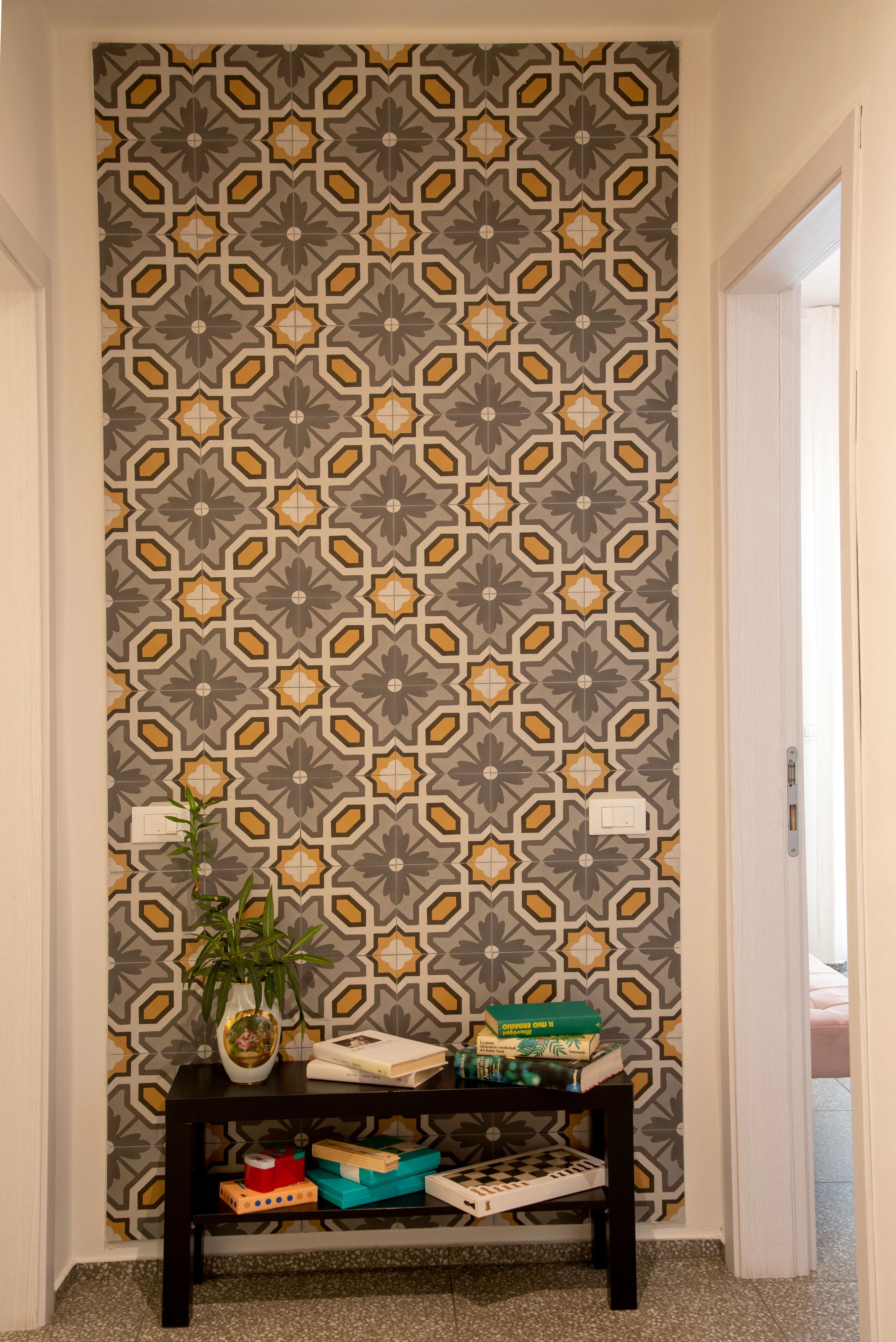 A hallway with a patterned wallpaper, a small table with a potted plant, and a shelf with various items.