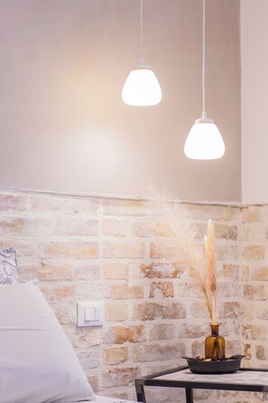 A room with a brick wall, a white bed, a small table with a vase, and two hanging pendant lights. - B&B Fontanella32  (Porto Sant'Elpidio)