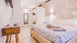 A bedroom with a bed, a bedside table, a mirror, and a wall-mounted TV.