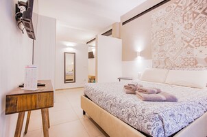 A bedroom with a bed, a bedside table, a mirror, and a wall-mounted TV.