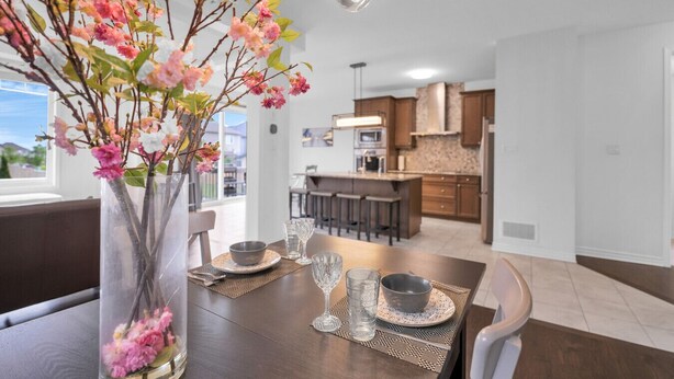 Uma sala de jantar com uma mesa posta para dois, um vaso com flores e vista para a cozinha ao fundo.