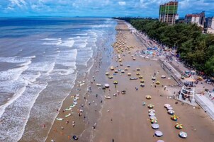 Una playa con sombrillas y gente, una costa y edificios al fondo.