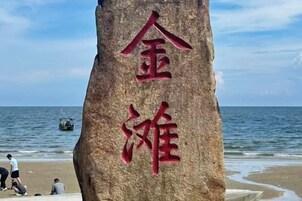 Una gran roca con caracteres chinos, una playa y el océano al fondo.