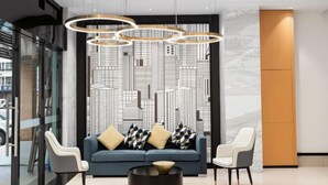 Un hall d’entrée moderne avec un canapé bleu, deux fauteuils, une table basse ronde et un mur décoré d’un paysage urbain.