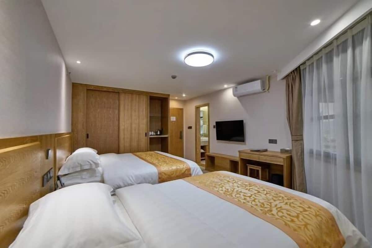 Ein Hotelzimmer mit zwei Betten, einem Schreibtisch, einem Fernseher und einer Klimaanlage.