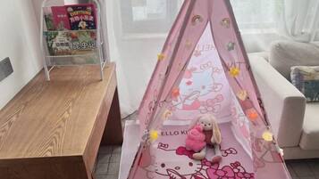 A room with a wooden bench, a pink tent-like structure with a stuffed toy, and a magazine rack.