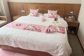 A neatly made bed with a pink and white bedspread, two pillows with a Hello Kitty design, and a Hello Kitty plush toy on the bed.