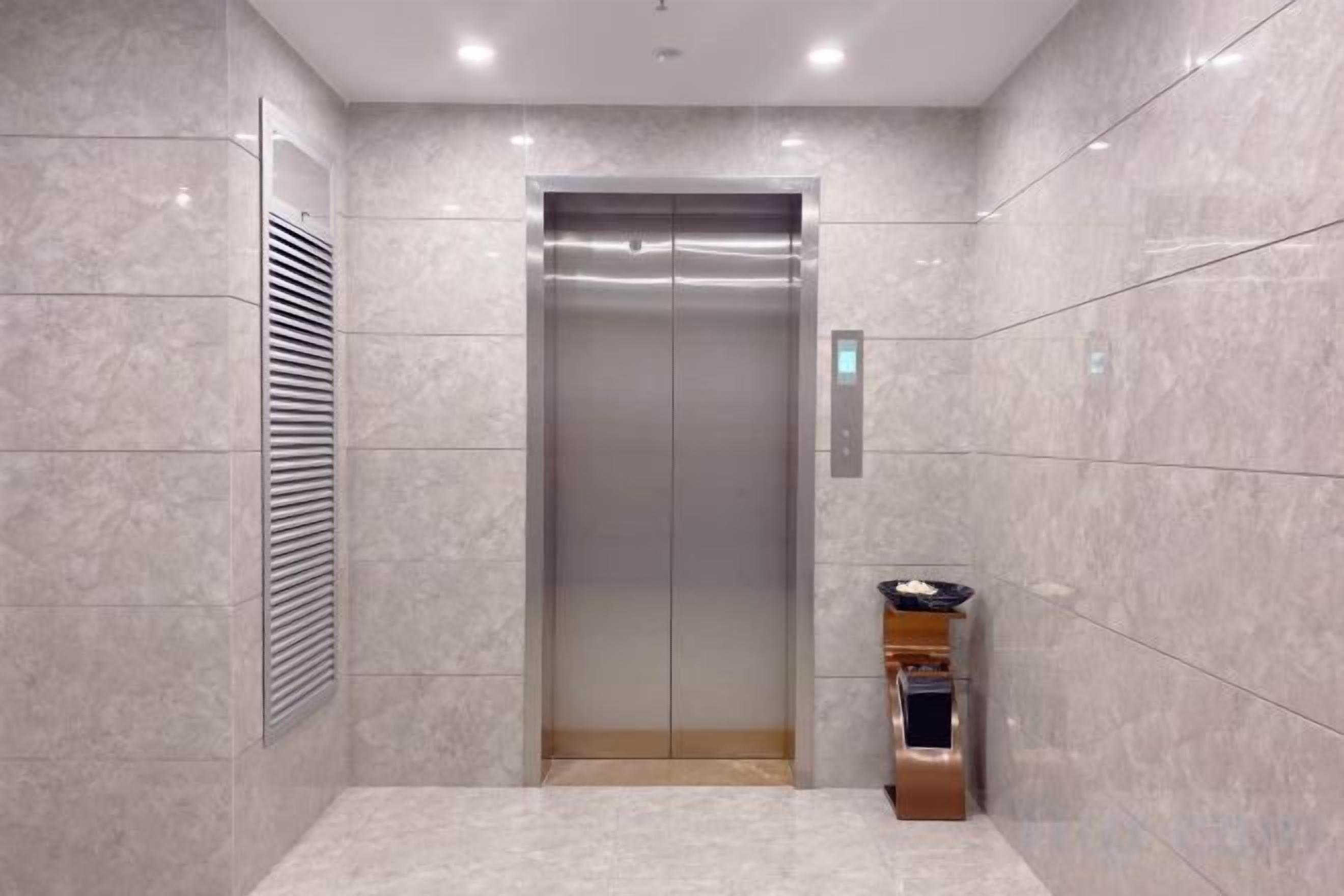 Un ascensor con detalles metálicos, un respiradero empotrado en la pared y un pequeño estante con dispensador de agua.