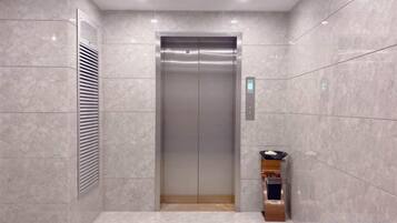 Un ascensor con detalles metálicos, un respiradero empotrado en la pared y un pequeño estante con dispensador de agua.