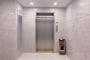 An elevator with a metallic finish, a wall-mounted vent, and a small shelf with a water dispenser. - Landu shuntian Hotel (Baoshan)