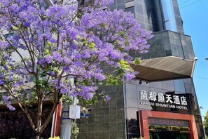 A hotel building with a sign in a foreign language, a tree with purple flowers in front, and a clear sky. - Landu shuntian Hotel (Baoshan)