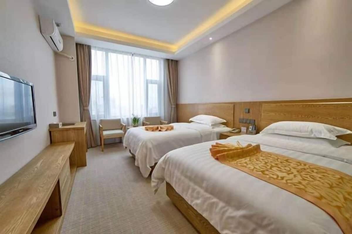 Ein Hotelzimmer mit zwei Betten, einem Fernseher, einem Schreibtisch und einem Sessel.