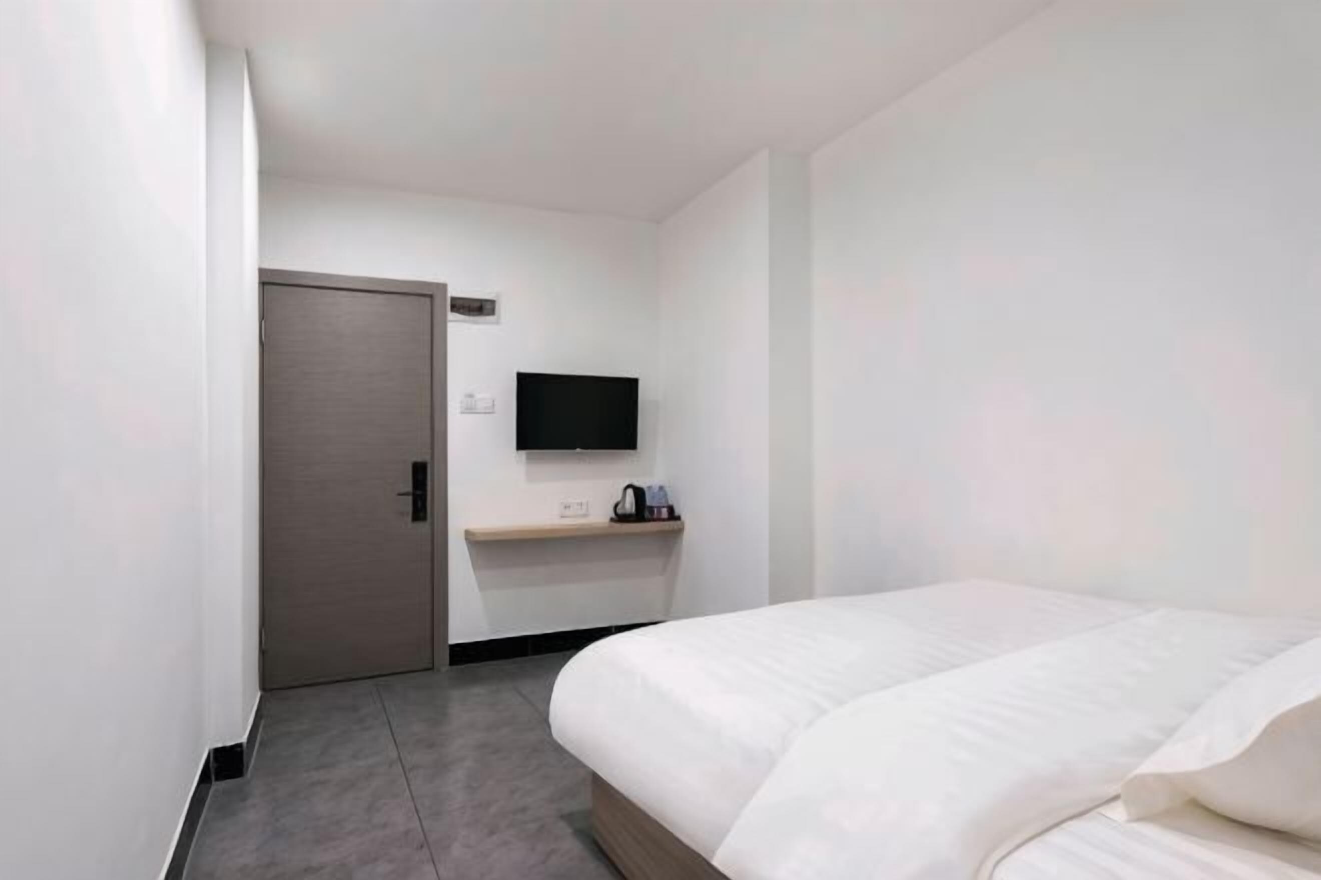 A hotel room with a bed, a TV mounted on the wall, a door, and a small table with a kettle.