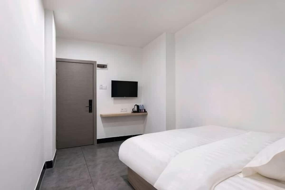 A hotel room with a bed, a TV mounted on the wall, a door, and a small table with a kettle.