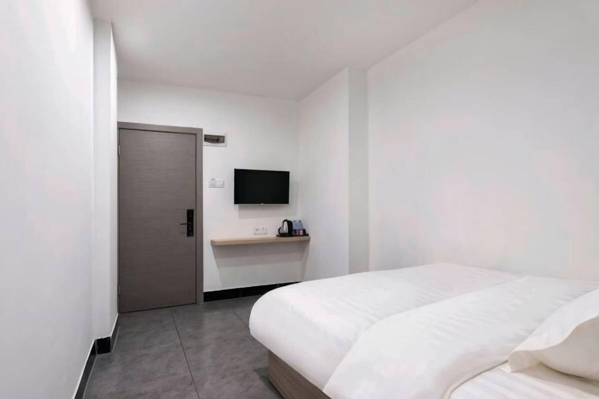 A hotel room with a bed, a TV mounted on the wall, a door, and a small table with a kettle.