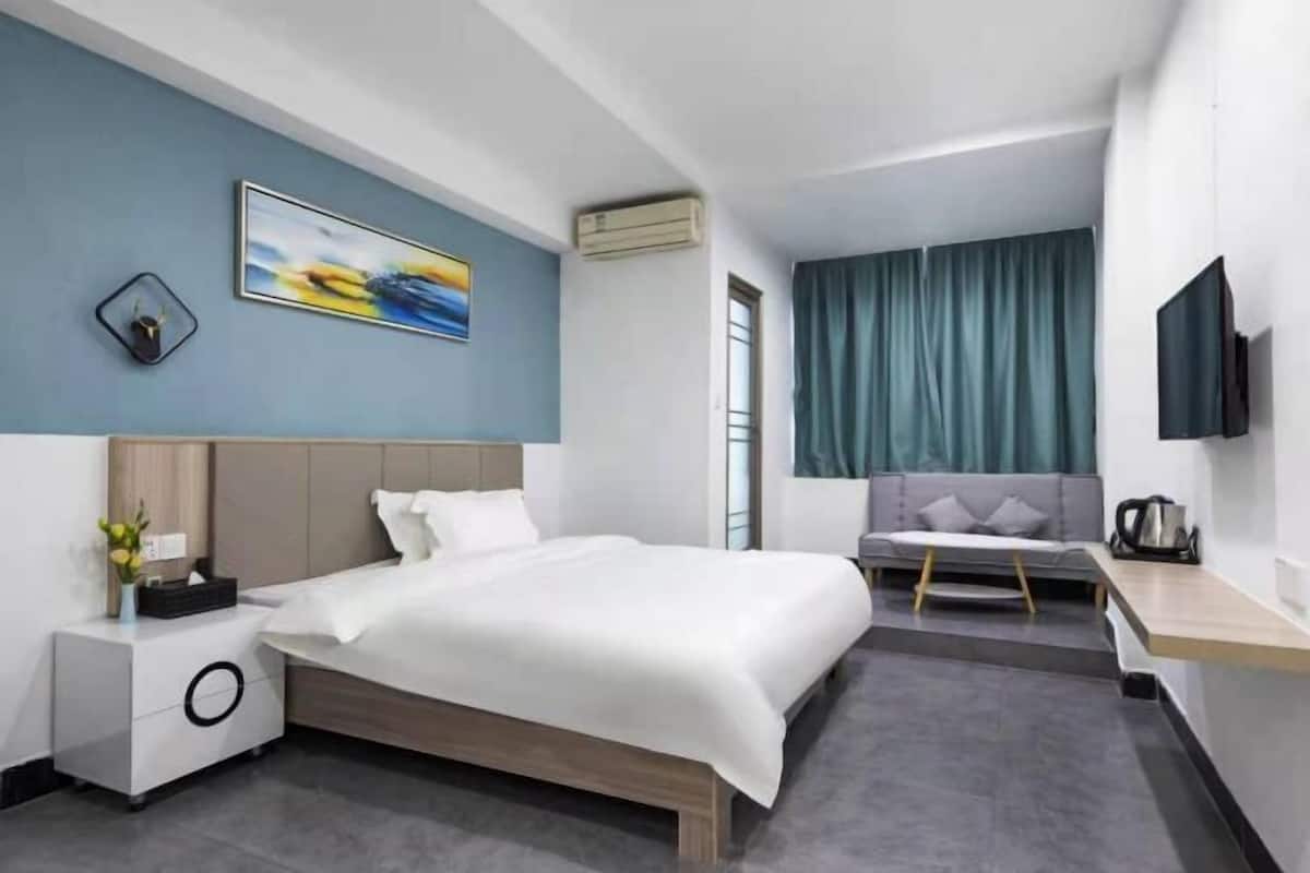 A modern hotel room with a bed, bedside table, TV, and a view of the city.