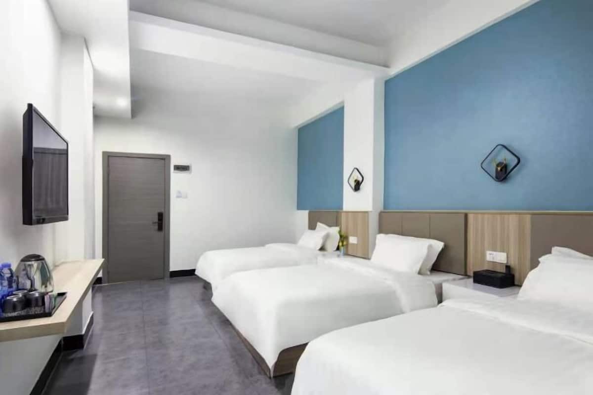 A hotel room with three beds, a desk with a coffee maker, a TV, and a door.