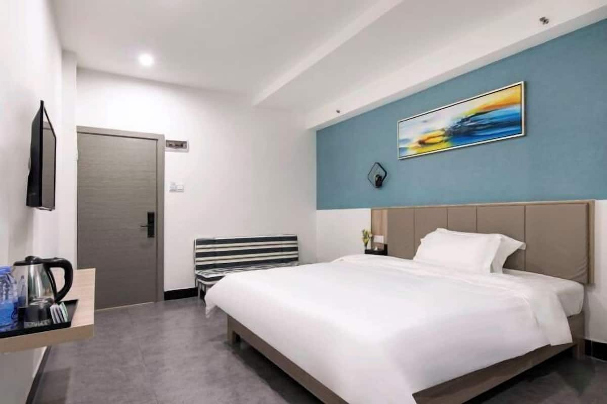 A modern hotel room with a large bed, a flat-screen TV, a coffee maker, and a painting on the wall.