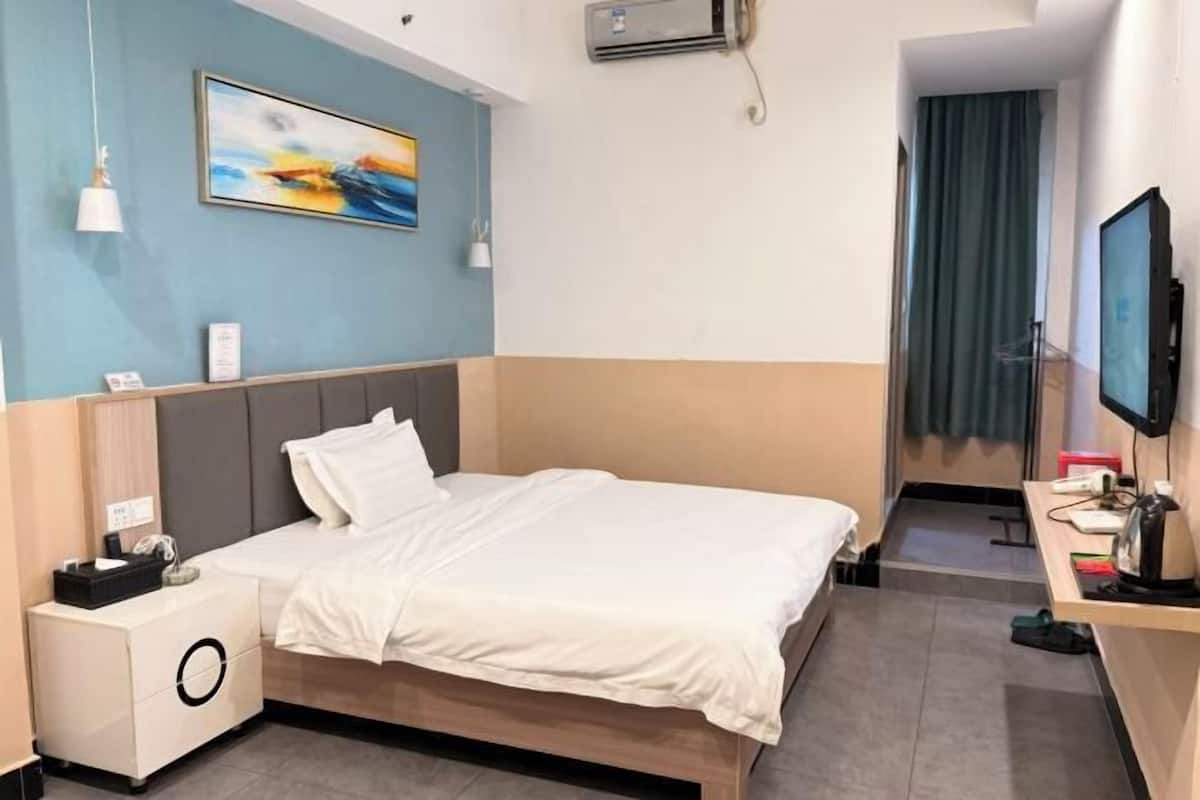 A hotel room with a bed, a desk, a television, and a painting on the wall.