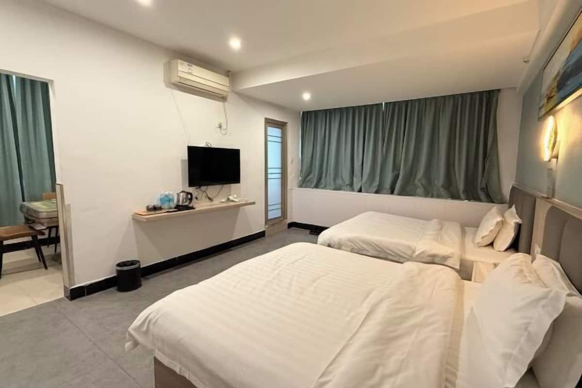 A hotel room with two beds, a desk, a television, and a window with curtains.