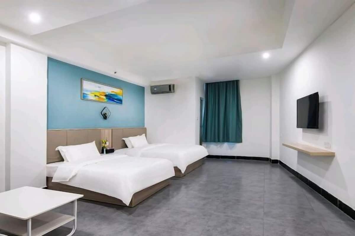 A hotel room with two beds, a TV, a desk, and a painting on the wall.