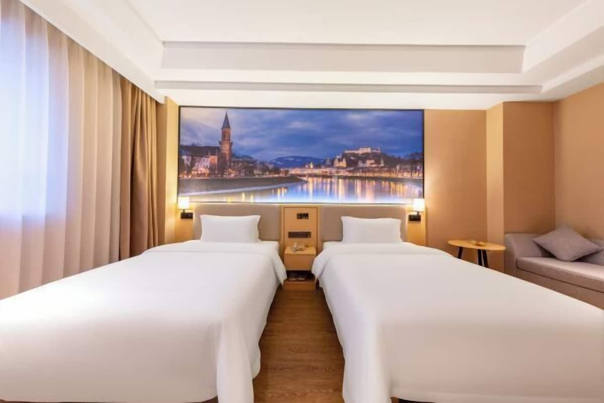 A hotel room with two beds, a sofa, a nightstand, and a large window with a cityscape view.