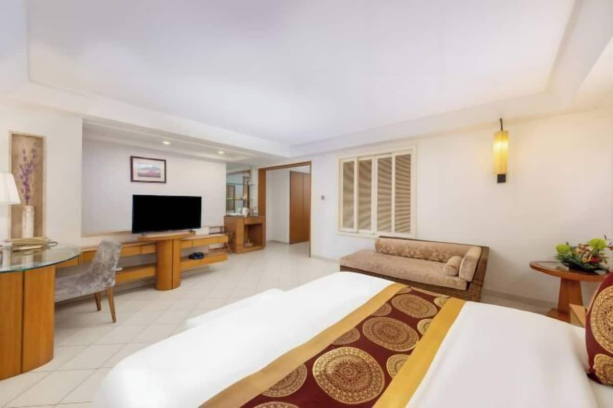 A hotel room with a bed, a desk with a TV, a sofa, and a window with blinds.
