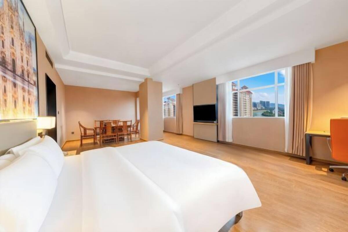 A hotel room with a large bed, a desk, a chair, a TV, and a window with a city view.