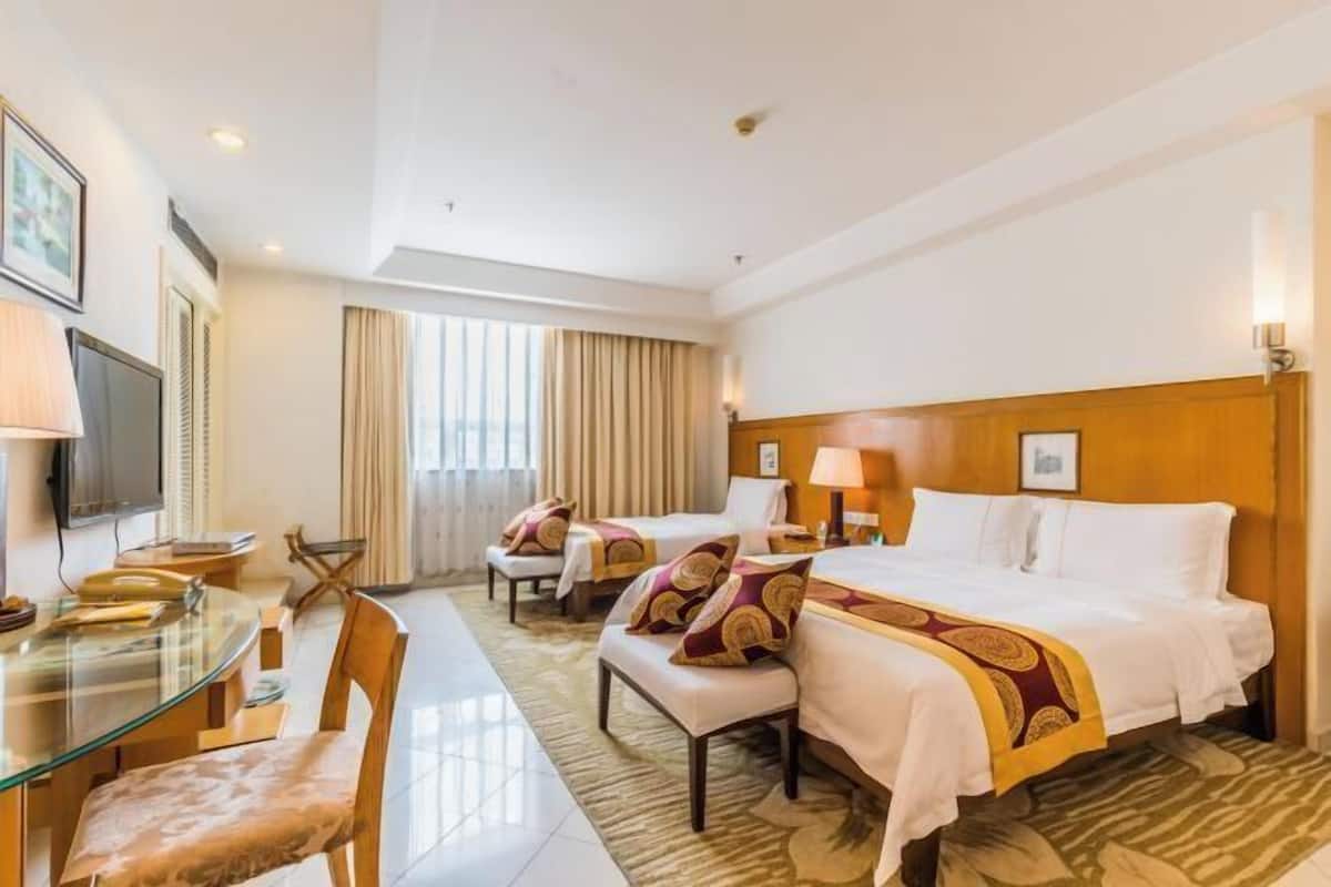 A hotel room with a bed, two bedside tables, a TV, a glass table with chairs, and a window with curtains.