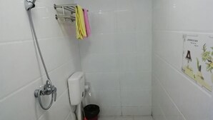 A small, white-tiled bathroom with a toilet, a hand dryer, a paper towel dispenser, a bucket, and a showerhead. - Qingliangzhai Liu Yinong Family Lodging (Wuhan)