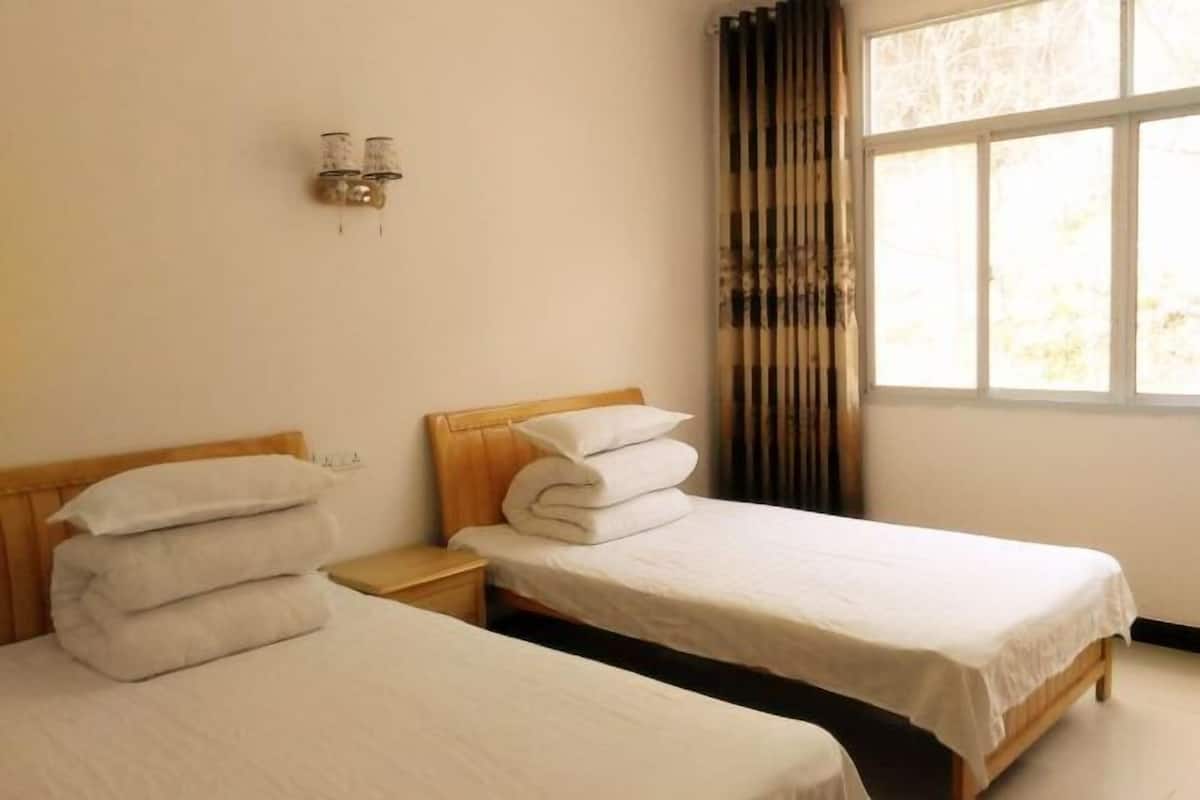 A hotel room with two single beds, a nightstand, and a window with curtains.