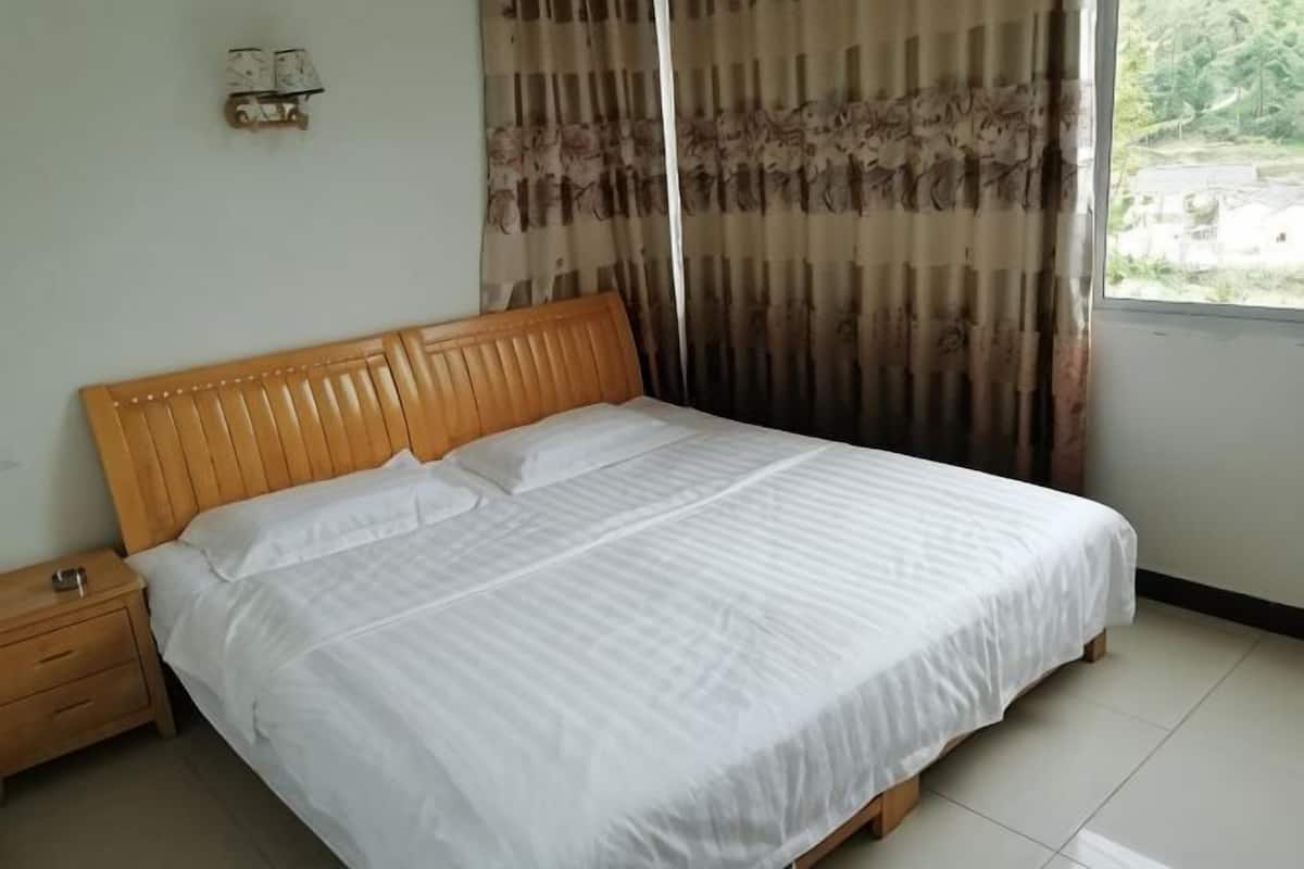A bedroom with a wooden headboard, a white bedspread, a nightstand, and a window with curtains.