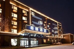 A multi-story hotel with illuminated signage, a covered entrance, and a parking area. - Xiya Hotel (Xiong'an New District Anxin Branch) (Anxin)