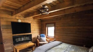 A wooden cabin room with a bed, a bench, a television, and a window.
