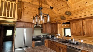 A spacious kitchen with wooden cabinets, granite countertops, stainless steel appliances, and a hanging light fixture.