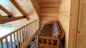 A wooden cabin with a loft-style bed, a wooden deck, and a door.