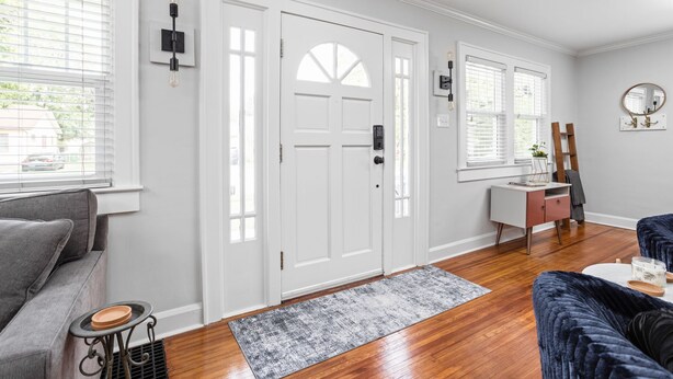 Una sala moderna con un sofá gris, un sillón azul, una mesita con un cuenco y un escritorio blanco con un espejo.