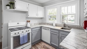 Una cocina moderna con armarios blancos, horno empotrado y encimera de granito.