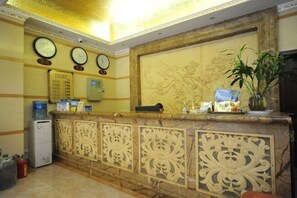 A reception area with a marble counter, decorative panels, clocks, a water dispenser, and a potted plant. - Haowanjia Hotel (Kunming)