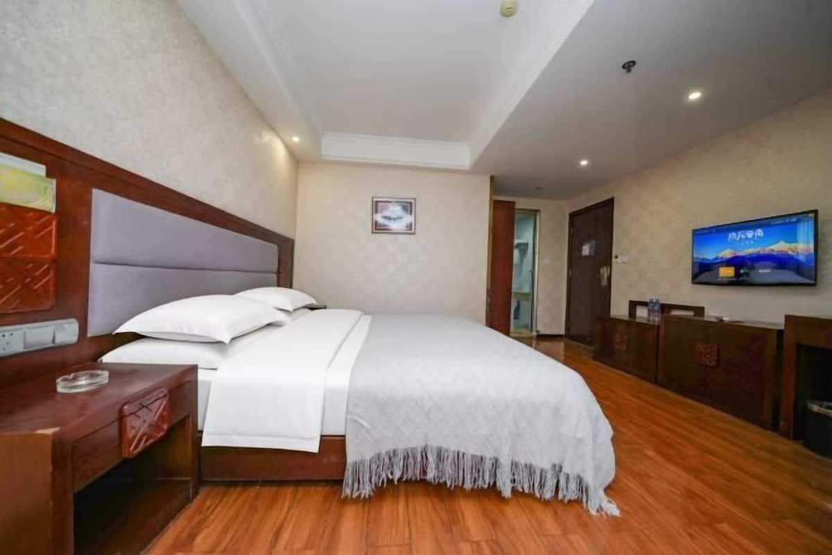 A hotel room with a bed, wooden floor, a TV on the wall, and a desk with a chair.
