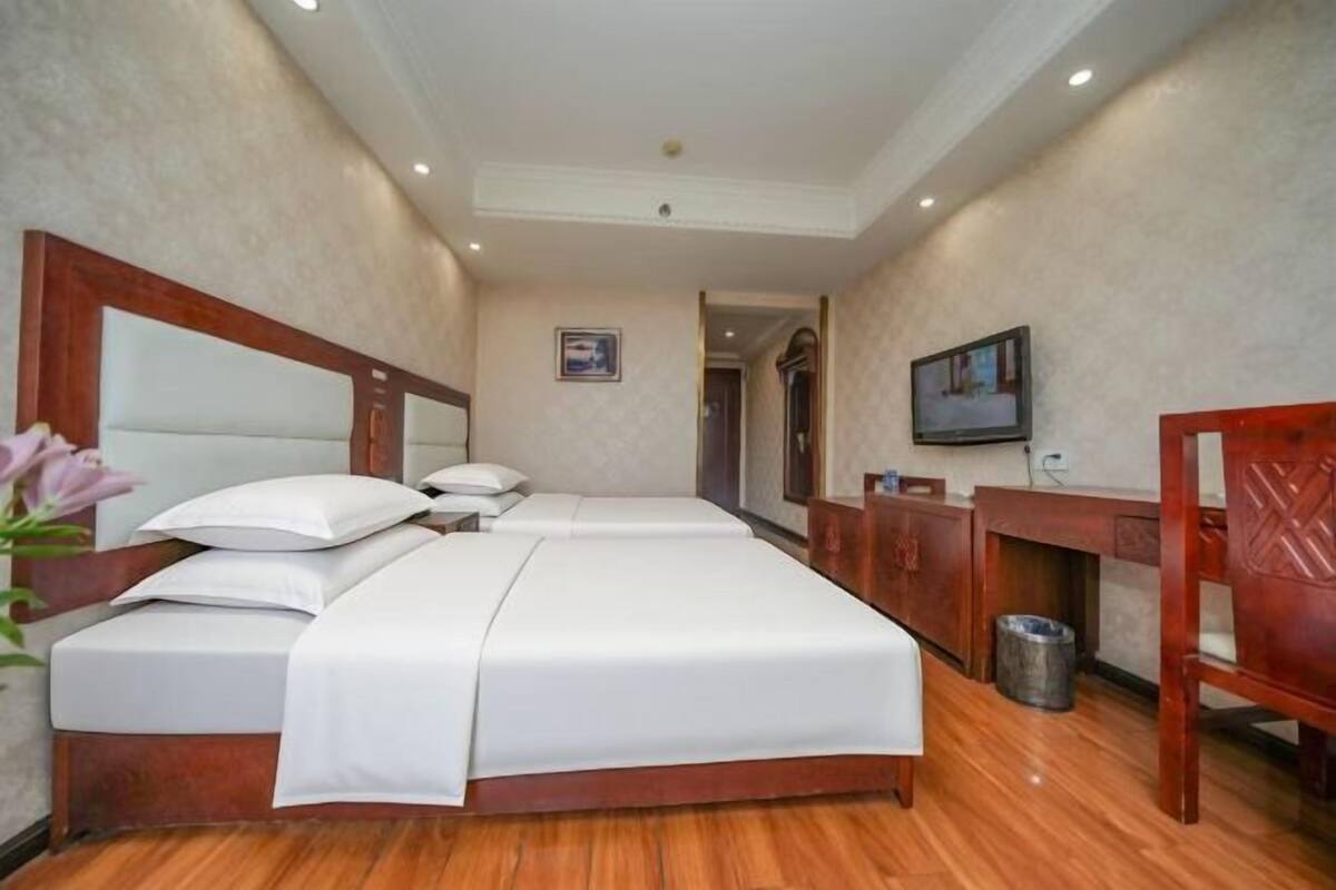 A hotel room with a large bed, a wooden headboard, a TV mounted on the wall, and a desk with a chair.