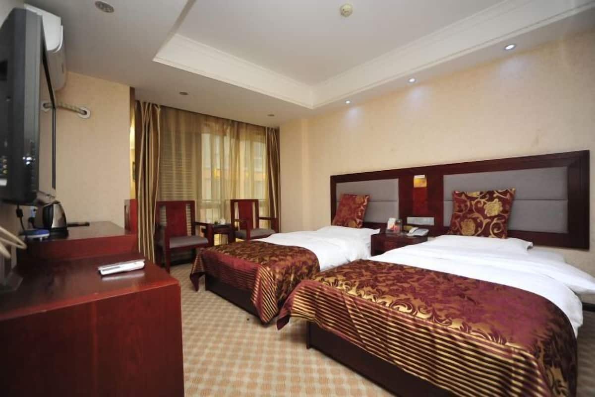 A hotel room with two beds, a desk, a television, and a window with curtains.
