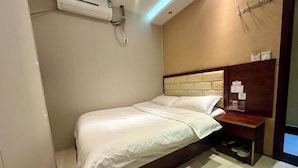 Een moderne hotelkamer met een bed, een vastgezet hoofdbord, een houten nachtkastje en een wandairconditioner.
