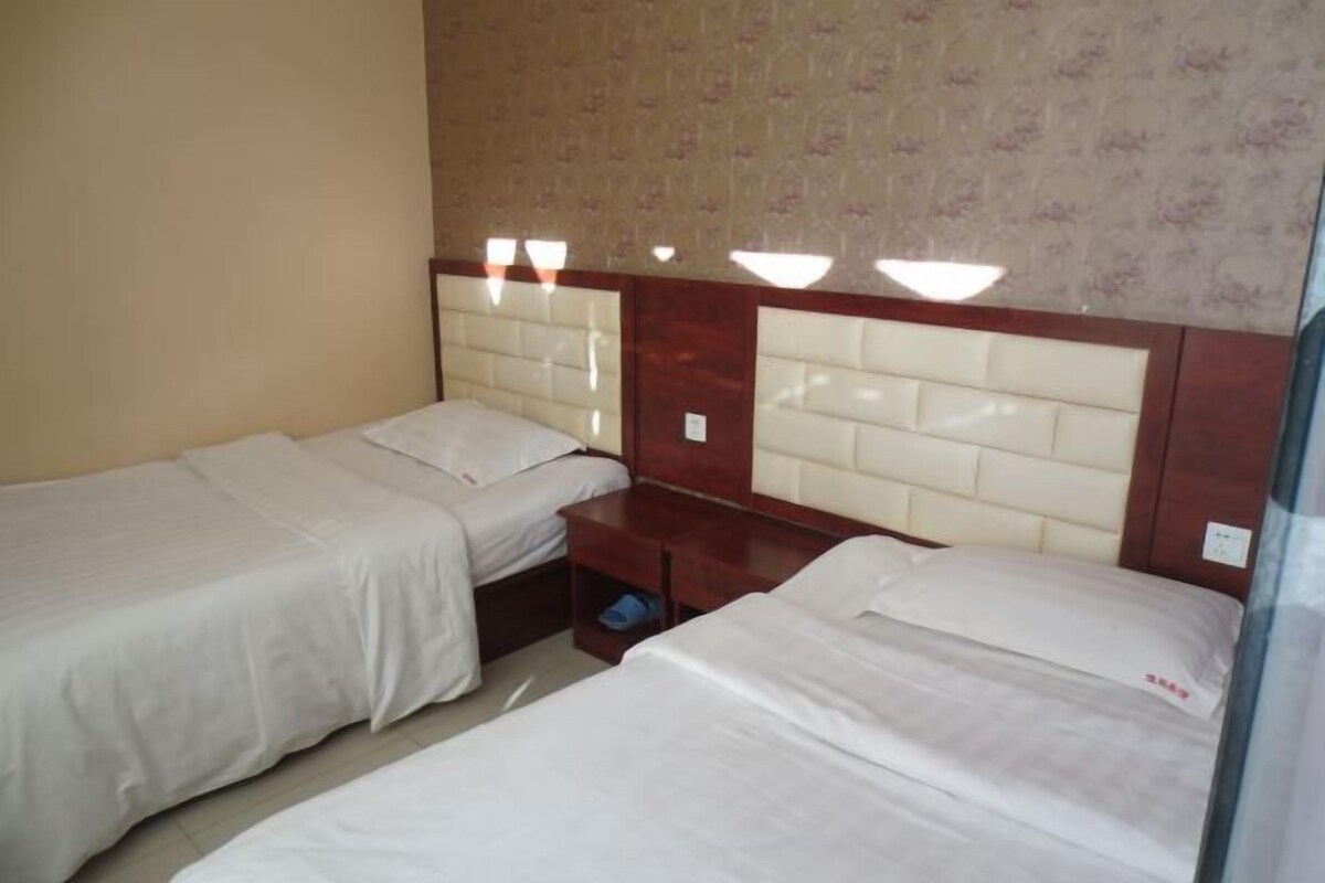 Een hotelkamer met twee enkele bedden, een houten hoofdbord en een klein nachtkastje met een lamp.