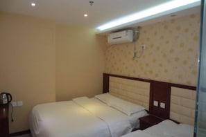 A hotel room with a bed, a bedside table, and an air conditioning unit mounted on the wall.