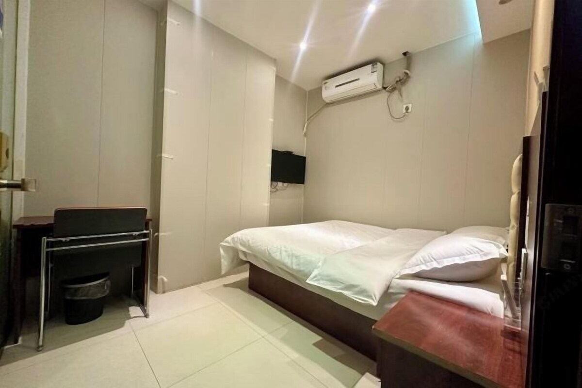 Een kleine, schone kamer met een bed, een bureau en een wandairconditioning.