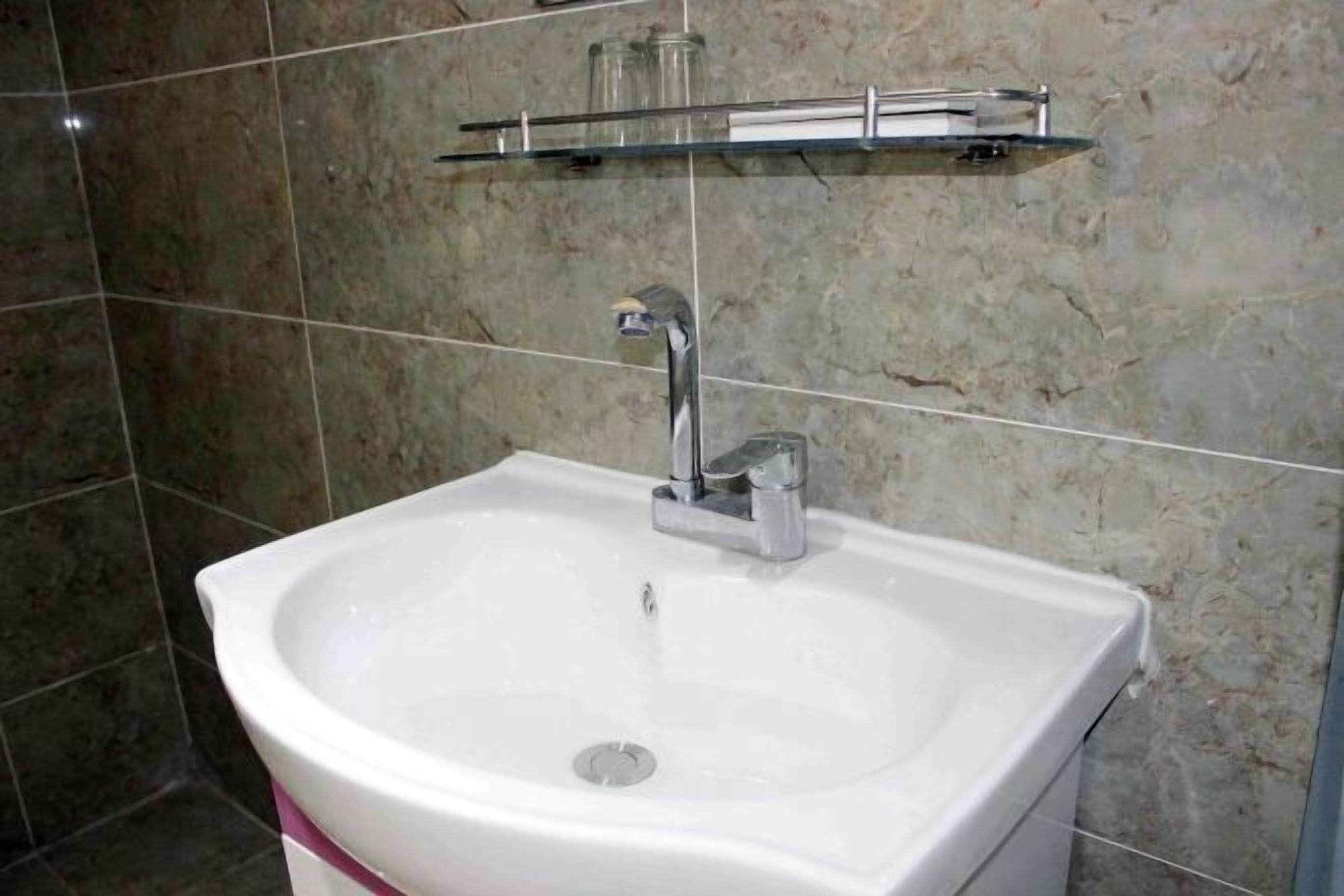 A bathroom with a white sink, a chrome faucet, and a glass shelf above the sink.