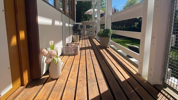 A wooden deck with a white railing, a potted plant, and a bench.